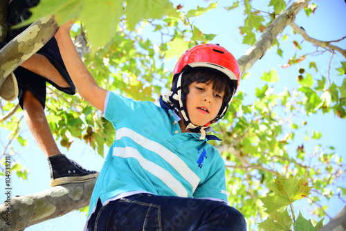 Bopy with red helmet climbing a tree photo