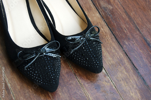 Women's shoes with black bow with a wooden floor in the background.