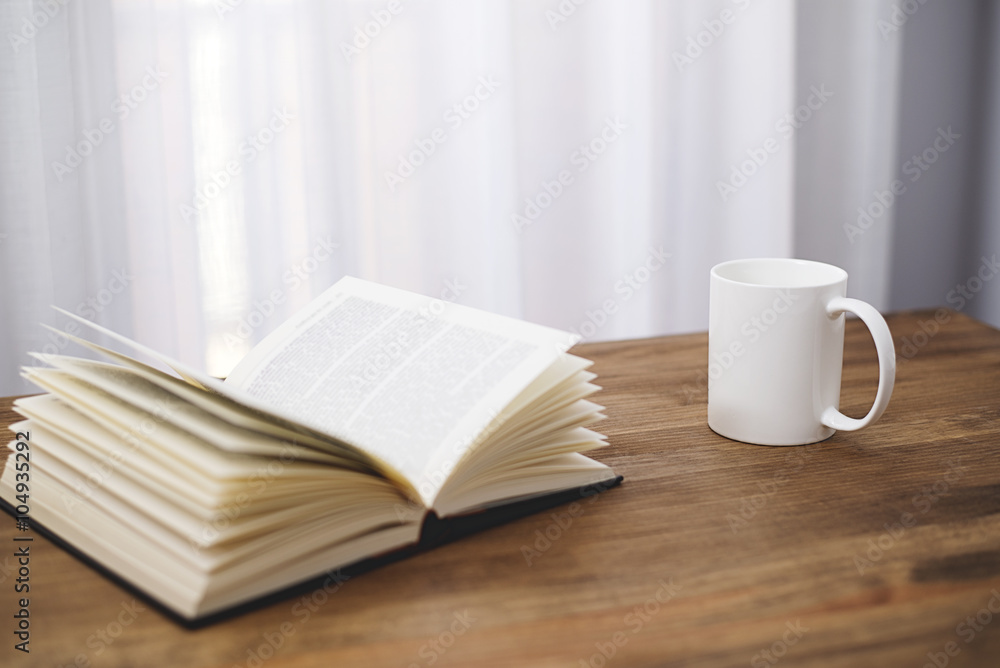 Naklejka premium White cup of coffee with a book on wooden table.