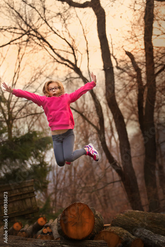 a girl wearing a pink sweatshirt jumping off a fallen tree