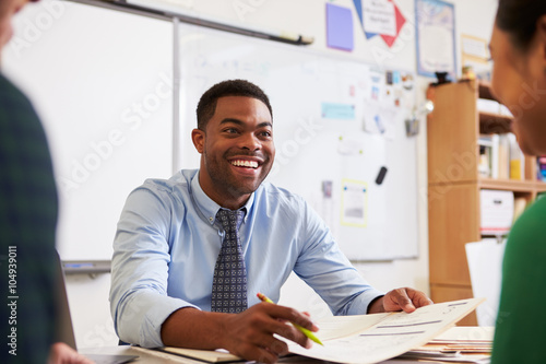 Happy teacher at desk talking to adult education students