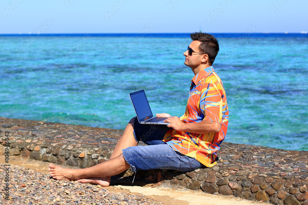 young man, freelancer, working at his laptop computer at the sea 