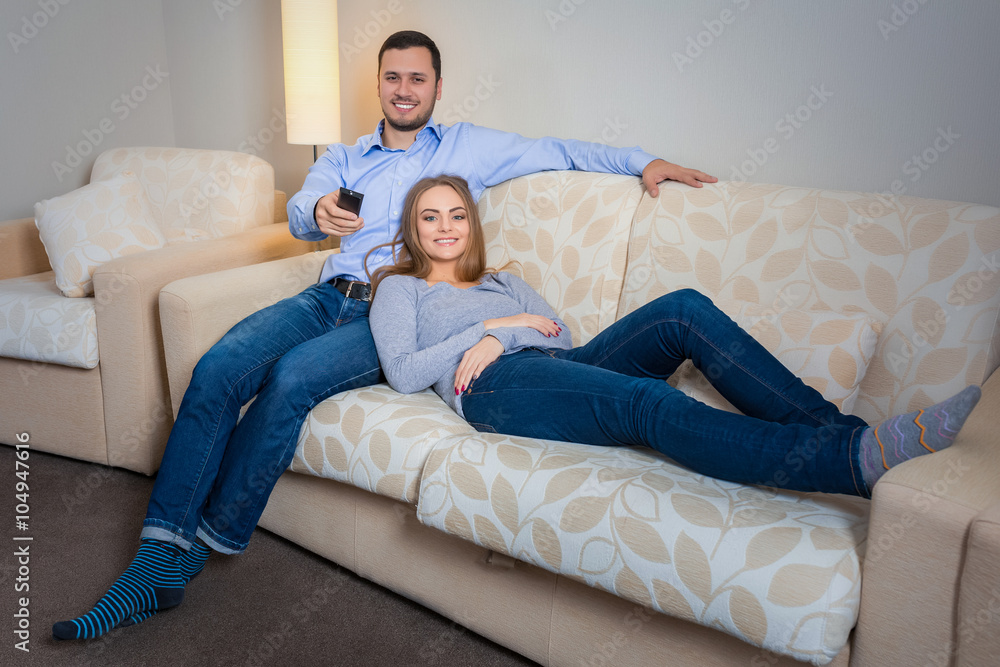 Happy couple sitting on sofa watching television together Happy couple sitting on sofa watching television together