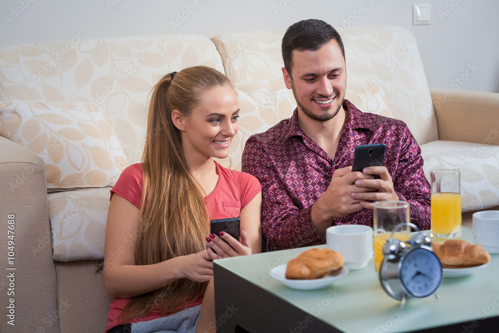 Cute young couple having breakfast, photographs at mobile phone Cute young couple having breakfast, photographs at mobile phone