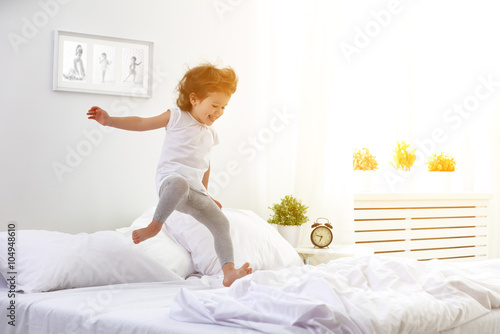 happy child girl jumps and plays bed