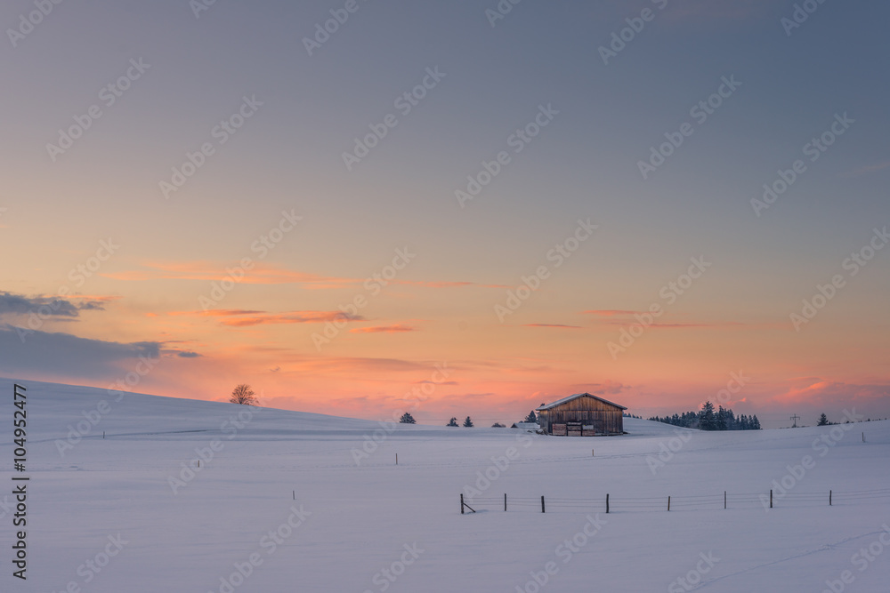 lonely chalet on snowy meadow at winter sunset and orange clouds