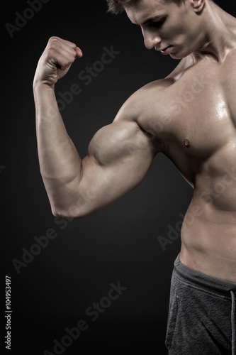 Fitness man showing his triceps, biceps muscles on black background