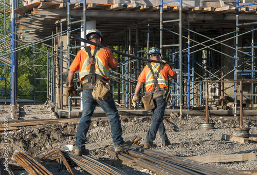 Obraz na plátne Two construction workers carrying metal rods on their shoulder