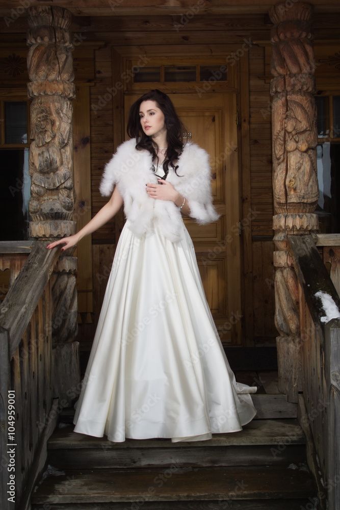 The bride in a fur cape on a porch of a wooden house