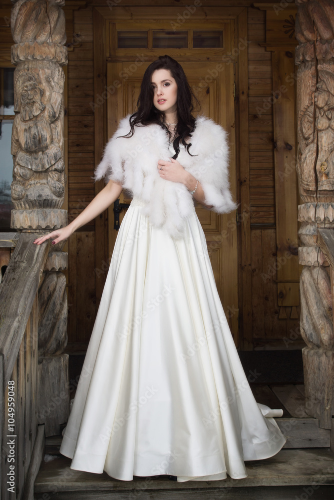 The bride in a fur cape on a porch of a wooden house The bride in a fur cape on a porch of a wooden house