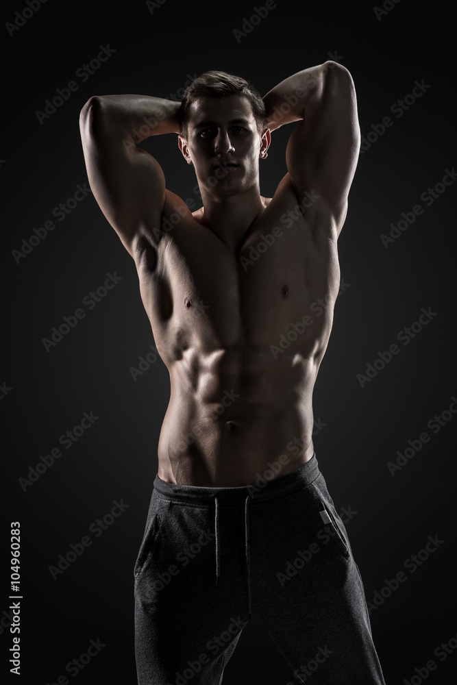 Fototapeta premium Sexy shirtless bodybuilder posing, looking at camera on black background.