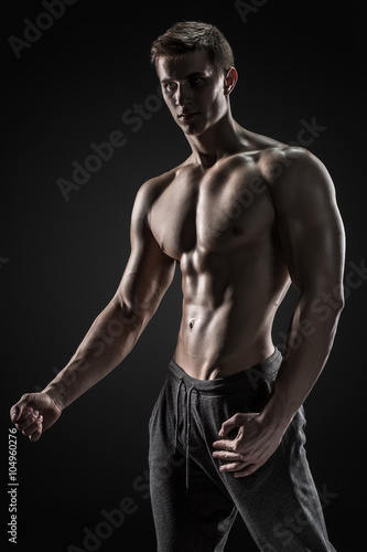 Sexy shirtless bodybuilder posing, looking at camera on black background.