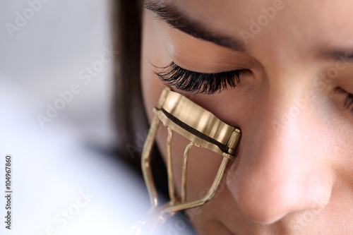 Woman corrects eyelashes with curling tongs, close up
