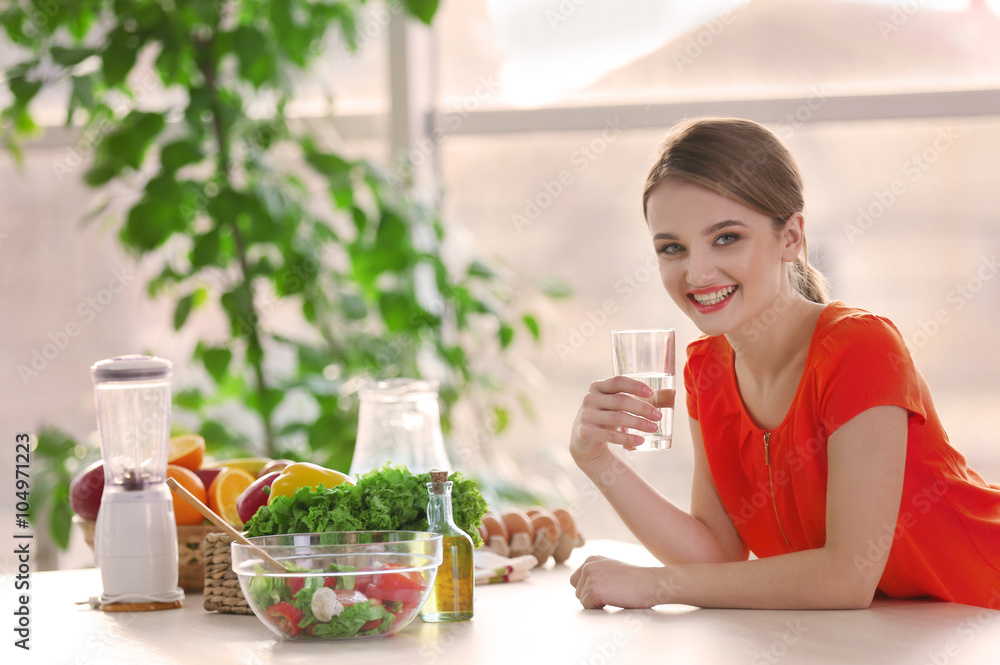 Young woman drinking water near table with fruits and vegetables in the kitchen Young woman drinking water near table with fruits and vegetables in the kitchen