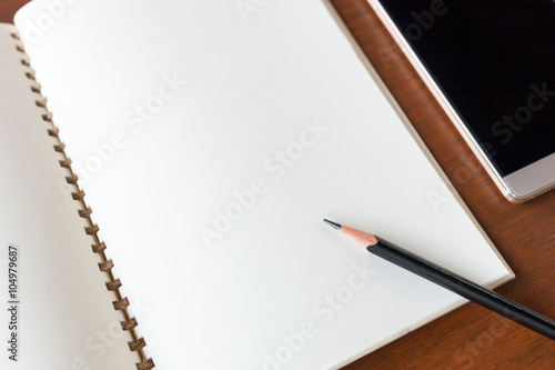 Blank note book with pencil and smartphone on wooden table backg