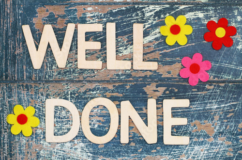 Well done written with wooden letters on rustic surface and colorful flowers
