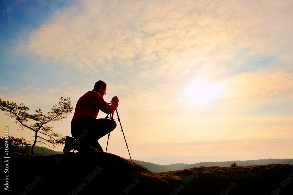 Nature photographer with tripod on cliff and thinking. Dreamy fogy valley below