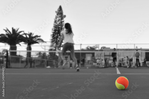 Tennis ball on background of young girl playing tennis on a court