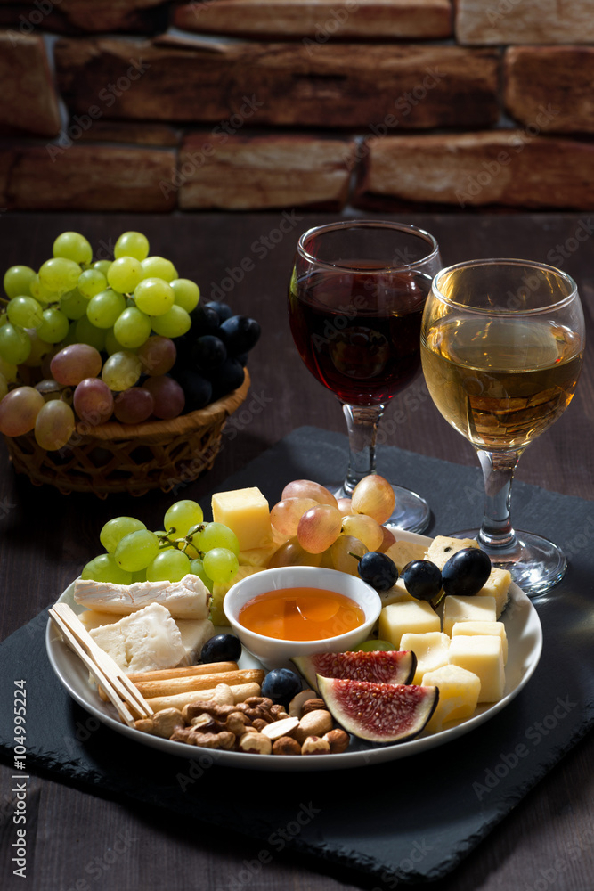 Plate with deli snacks and wine on a dark background, vertical