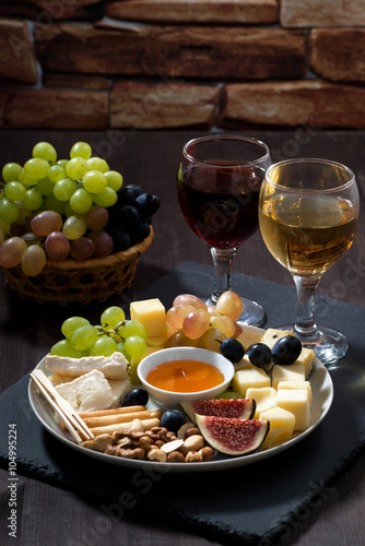 Plate with deli snacks and wine on a dark background, vertical