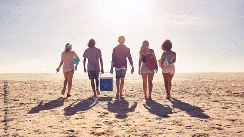 Foto Friends walking on the beach carrying a cooler box