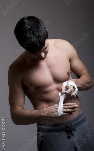 Young man putting tape in hands on a grey background