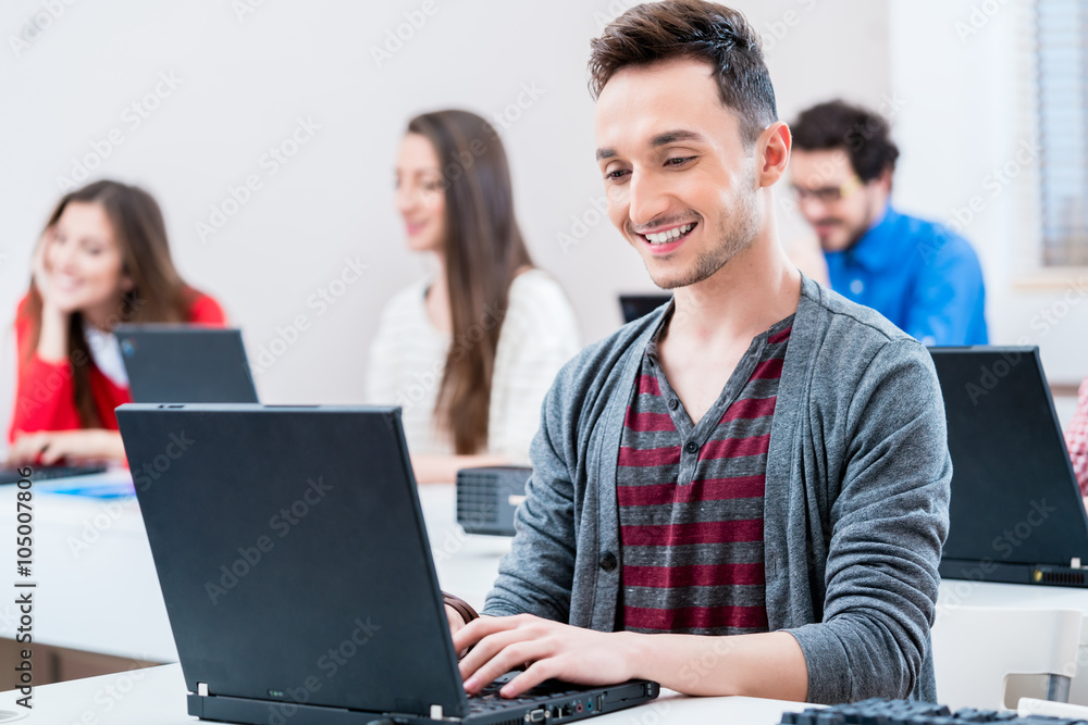Student arbeitet am Laptop Computer in Hochschule, weitere Frauen und Männer im Hintergrund
