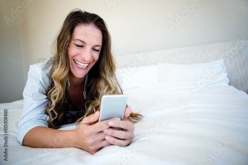 woman lying on her bed , laughing at her mobile phone