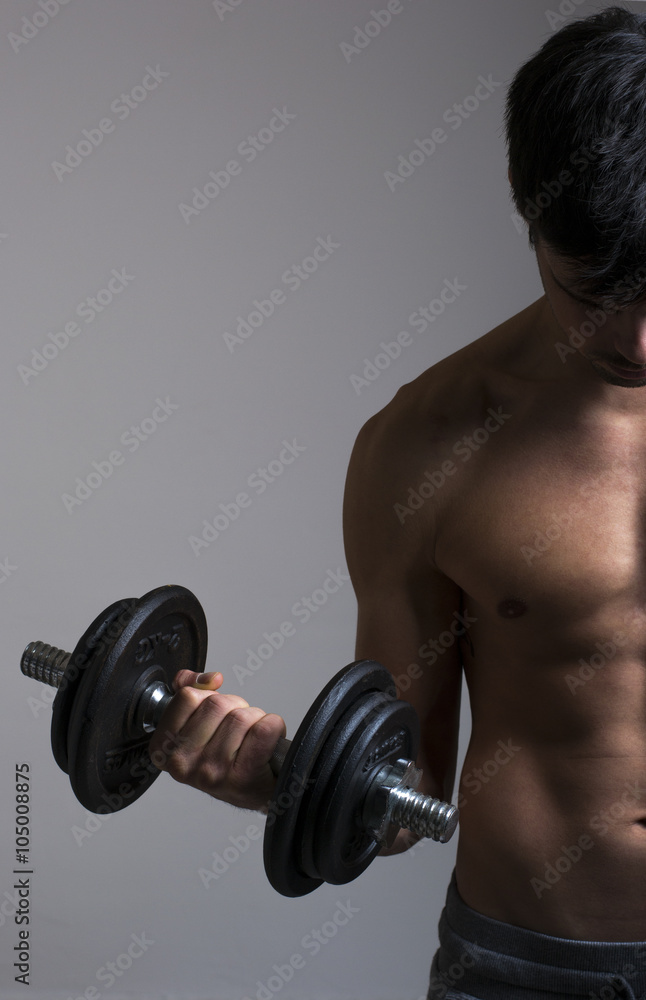 Strong young man with dumbbells on gray background