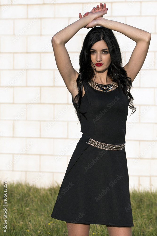 Azahara 1157 / Mujer joven morena de ojos marrones y con vestido negro  corto y zapatos negros con los brazos por encima de la cabeza mirando al  frente Stock Photo | Adobe Stock