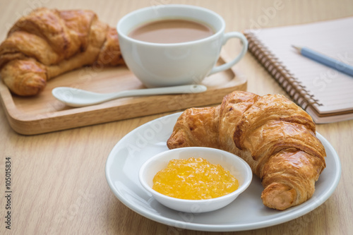 Croissant with jam on plate and coffee cup  book