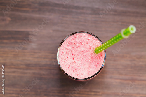A top view of a watermelon smoothie in a glass with tube on a wooden background