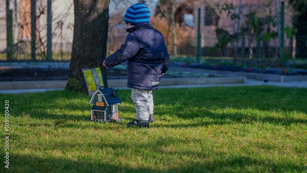 A little child is walking up to a small wooden house that is on the ground