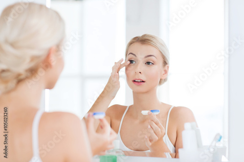 Fotografía young woman putting on contact lenses at bathroom