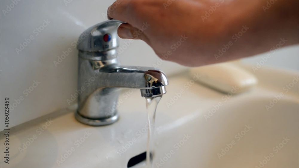Mann öffnet einen Wasserhahn beim Waschbecken Mann öffnet einen Wasserhahn beim Waschbecken