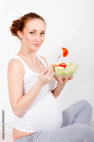 Beautiful young pregnant woman / teenager in white cloth eating healthy fresh salad with vegetables