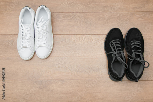 Two pairs of sneakers on a wooden background, black VS white concept