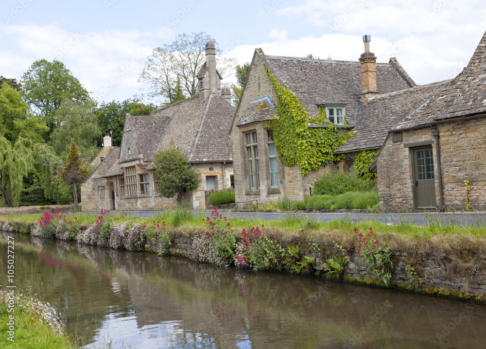 English stone cottages in the traditional Cotswold style along banks of  river  Eye with wild flowers