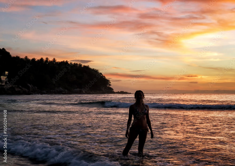 Young girl standing in the waves at sunset.