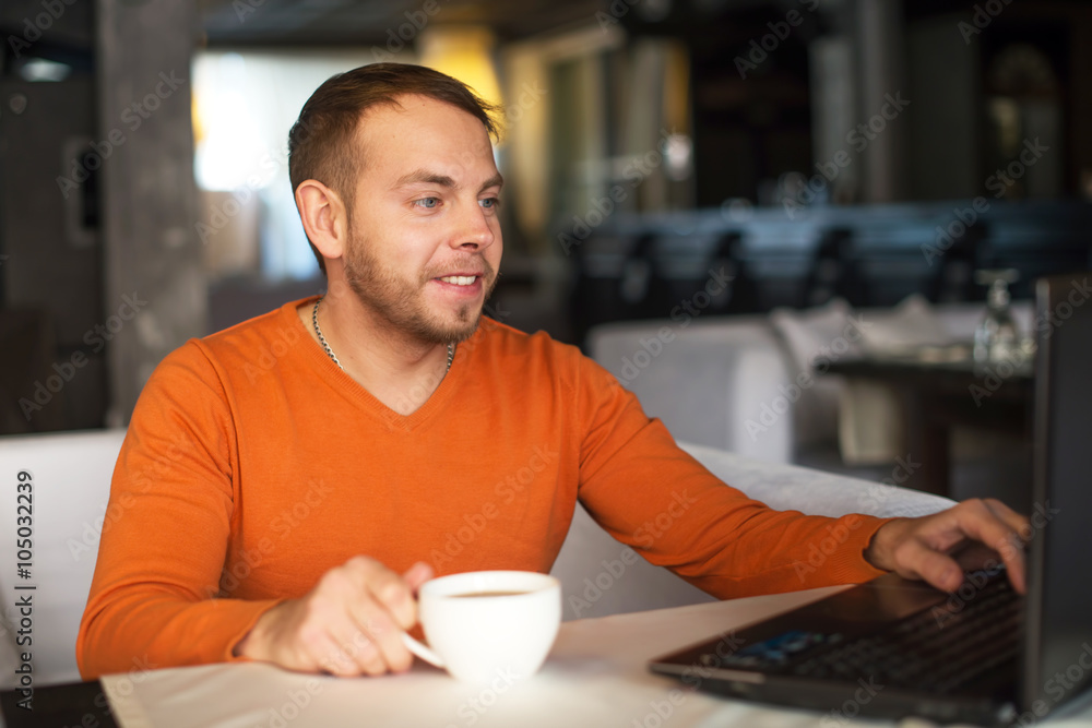 Handsome young man working on notebook, thinking, while enjoying coffee in cafe Handsome young man working on notebook, thinking, while enjoying coffee in cafe