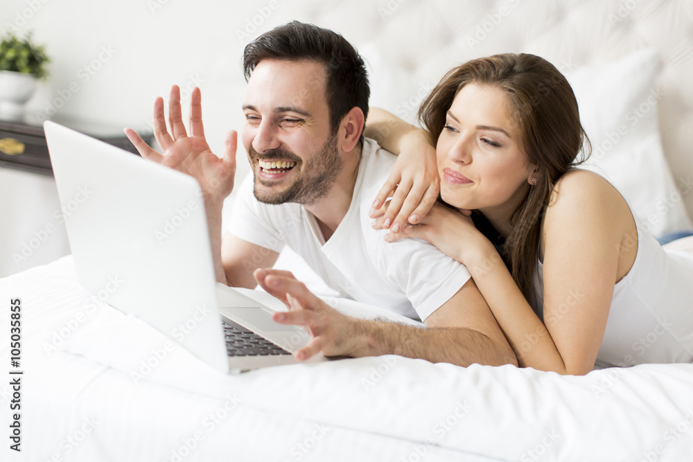 Fototapeta premium Young couple with laptop in the bed