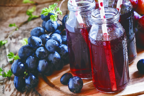 Fotografia Dark grape juice in glass bottles with straws, blue grapes, dark