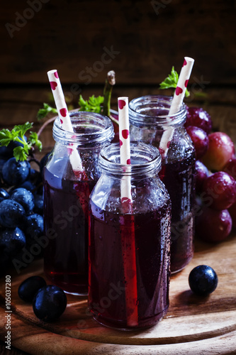 Fotografie Dark grape juice in glass bottles with straws, blue grapes, dark