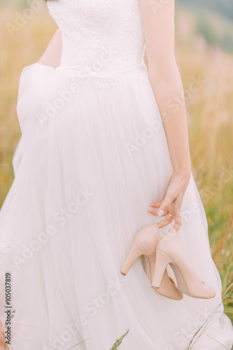 Beautiful bride walks with heels on hands. Green field close up  photo