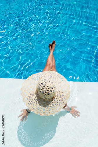 Woman sitting in a swimming pool in a sunhat