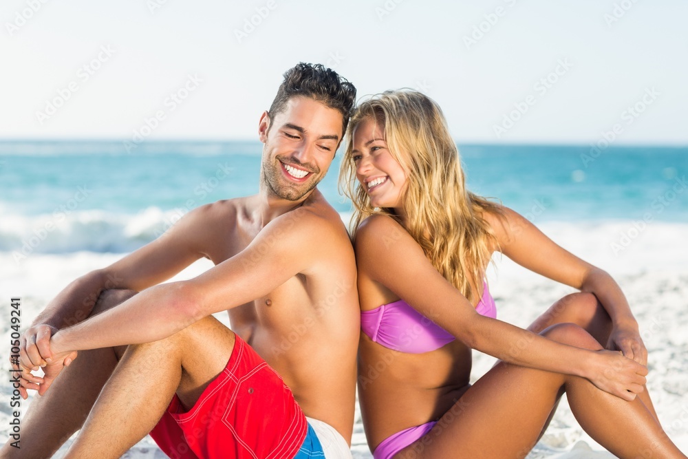 Happy couple sitting back to back on beach Happy couple sitting back to back on beach