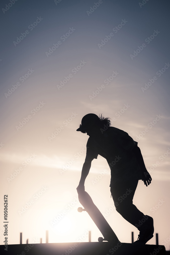 Teenager silhouette doing skateboard trick on ramp