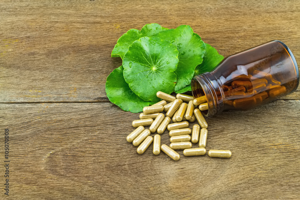 Green Asiatic Pennywort (Centella asiatica ) and  pills in black bottle on wooden background