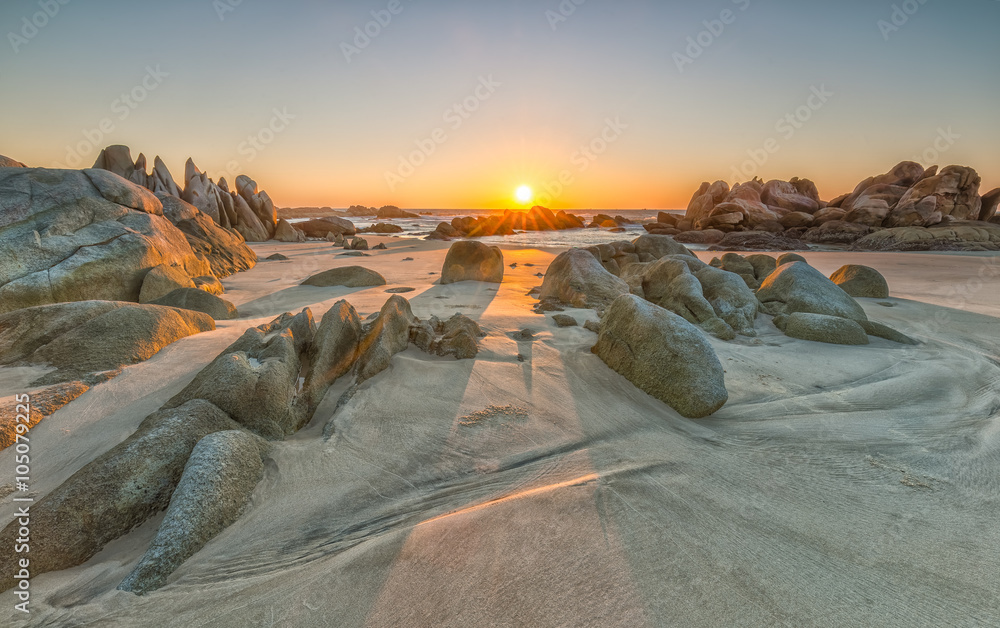 Naklejka premium The path of the rock into the sun rises with volcanic rocks on the sand overlooking the sea where the sun was rising star radiating beautiful to watch