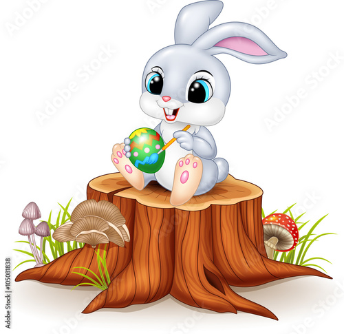 Cartoon Easter Bunny painting an egg on tree stump